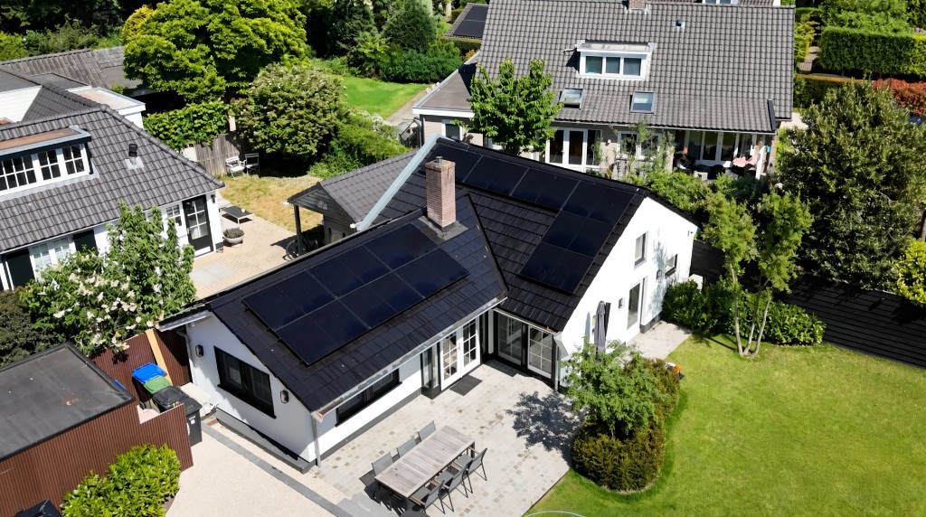 Luchtfoto van een woning met zwarte zonnepanelen op het dak